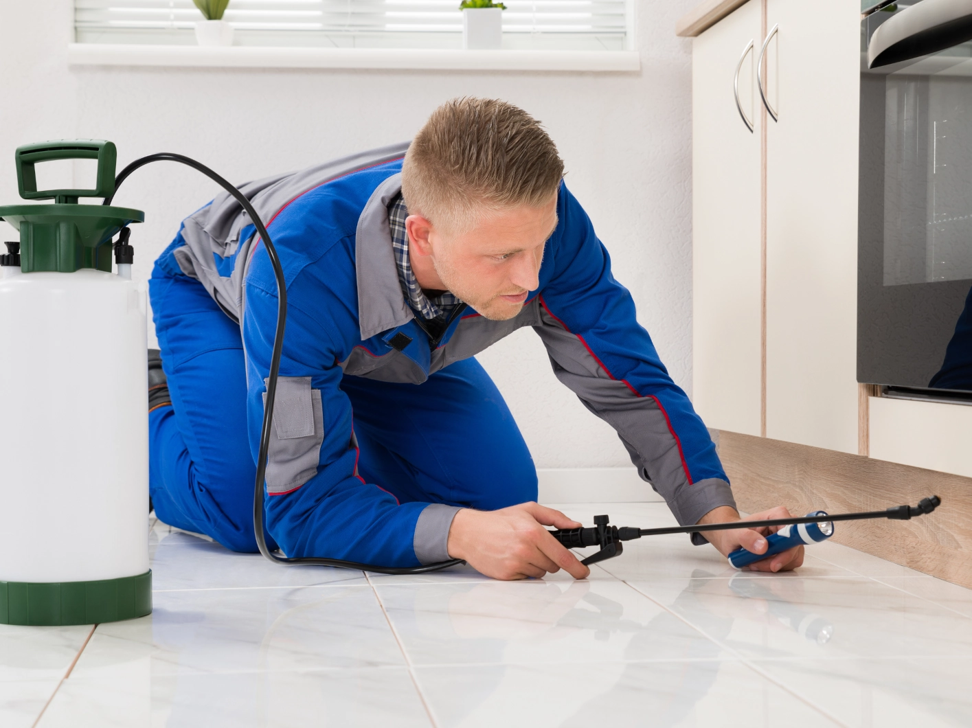 Pest control technician spraying under oven cabinet Pest control technician spraying under oven cabinet